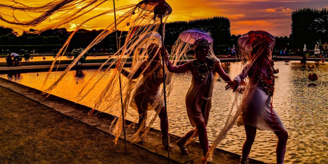 Drei Frauen in Quallenkostümen an einem Teich im Großen Garten Herrenhausen.